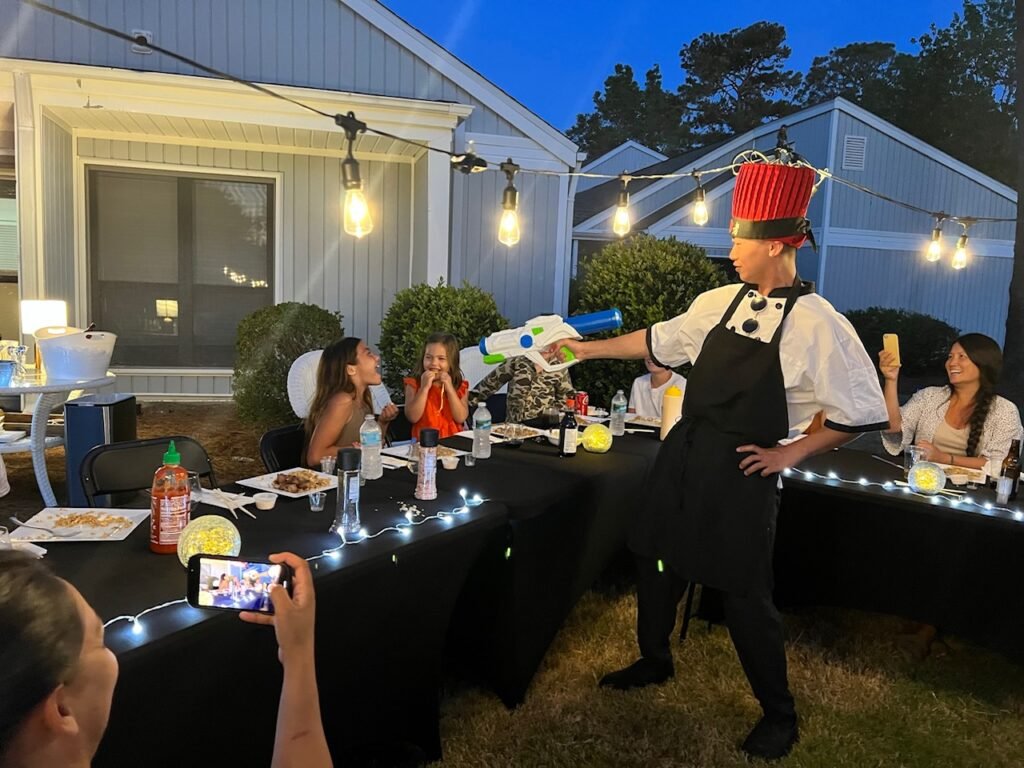 Hibachi dinner party with chef, grill and guests seated outdoors